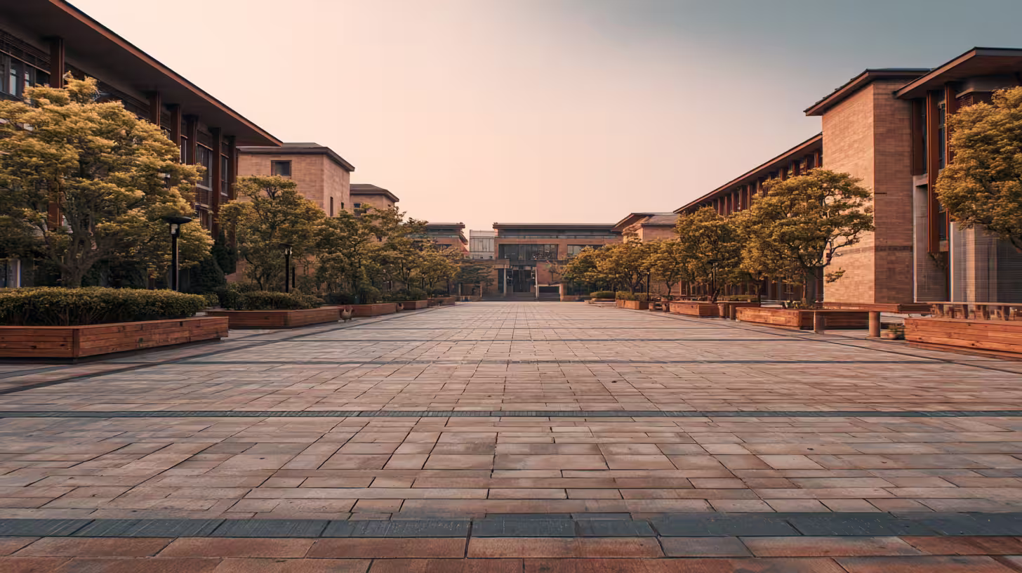 Wide brick-paved courtyard between modern brick university buildings with trees at golden hour