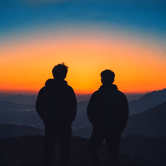 Silhouettes of two people watching the sunset over the mountains